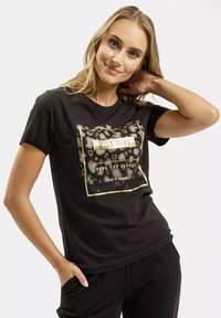 Czarny bawełniany t-shirt z grafiką w złotym i zwierzęcym wzorze oraz napisem "WILD GIRL STRONG AND FEARLESS CROSS JEANS." Krótkie rękawy.