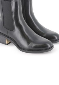 Botines de piel negra, con una superficie lisa, paneles laterales elásticos y un tacón bajo de bloque con un acento dorado.