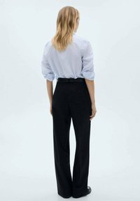 Light blue striped shirt with rolled sleeves, paired with high-waisted black wide-leg trousers. Smooth texture, tailored fit, and no visible patterns.