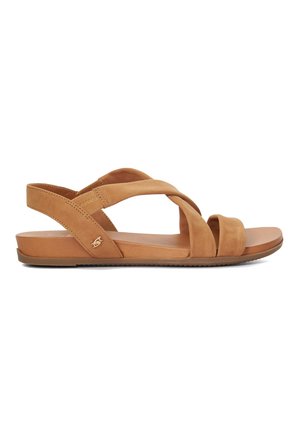 Sandales en suede tan avec des lanières croisées, semelle plate et un subtil détail de logo. Texture douce et design minimaliste.