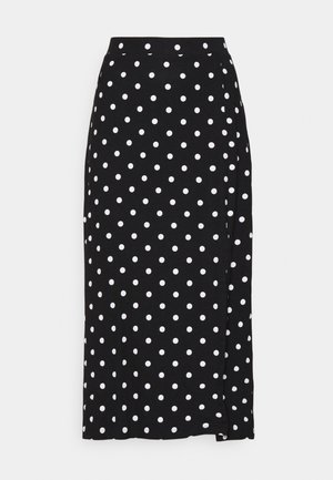 Jupe noire à pois blancs, faite en tissu doux. Elle présente une coupe droite et une fente en bas pour plus de liberté de mouvement.