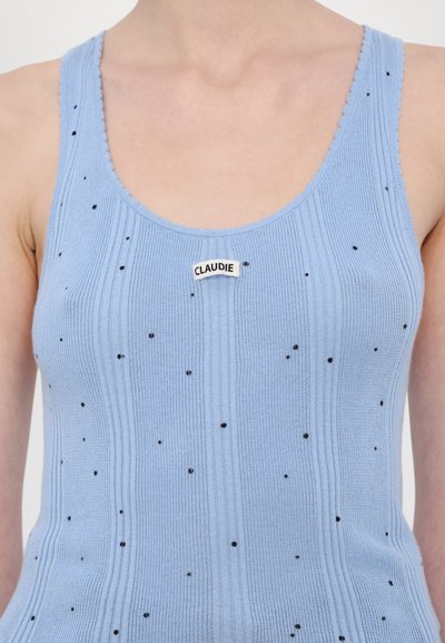 Lys blå ribbet tanktop med små svarte flekker; har en rund halsringning og en "CLAUDIE" etikett sentrert på brystet.