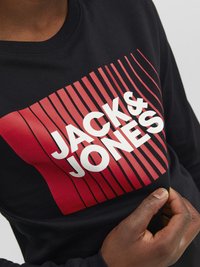 Crna dukserica dugih rukava s velikim crvenim grafikonom na kojem piše "JACK & JONES" i pozadinskim vertikalnim prugama.