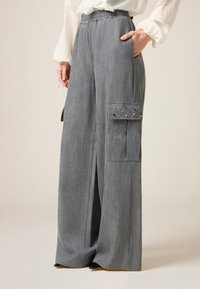 Grijze wijde broek met een elastische tailleband, zijzakken en een cargozak versierd met metalen studs. Gemaakt van een zachte stof.