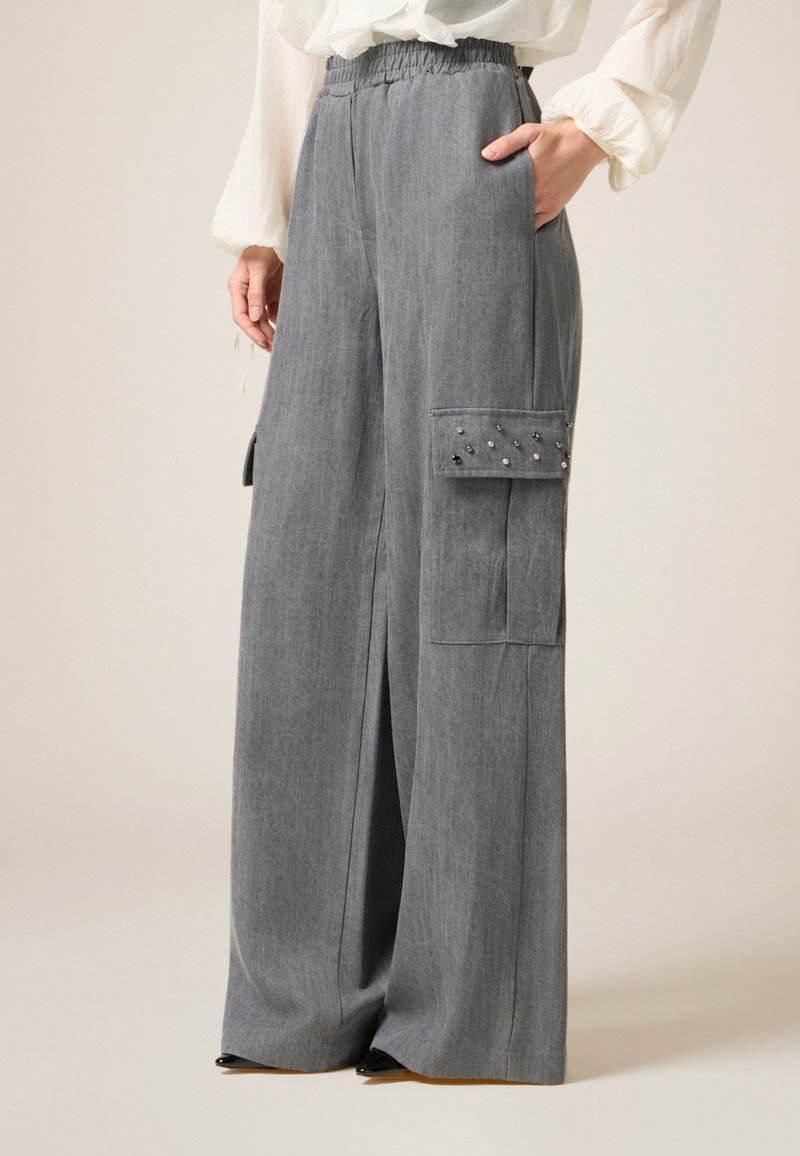 Grijze wijde broek met een elastische tailleband, zijzakken en een cargozak versierd met metalen studs. Gemaakt van een zachte stof.