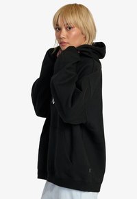Czarna, oversize bluza z kapturem, wykonana z bawełny, z przednią kieszenią, kapturem ze sznurkiem oraz ściągaczami na rękawach. Miękka, teksturowana tkanina.