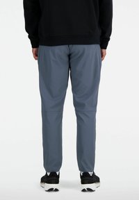Grå sportsbukser med en afslappet pasform, der har en glat struktur og en subtil glans. Sorte sneakers med hvide detaljer fuldender outfittet.
