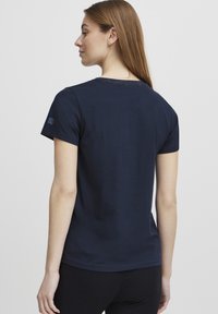 Camiseta de manga corta de color azul marino, hecha de algodón suave. Tejido ligero con cuello redondo y pequeño logotipo en la manga izquierda.