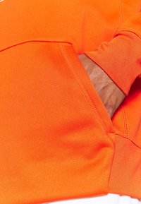 Sweat-shirt orange vif avec une texture douce, doté d'une poche avant et de poignets côtelés. Les coutures sont soigneusement réalisées.