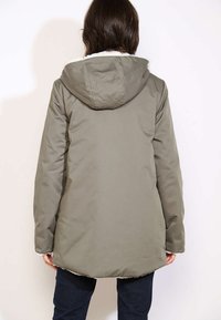 Olivgrüne, kapuzenjacke mit einem weichen, mit Fell gefütterten Kragen. Hat einen geraden Schnitt und einen etwas längeren Rückenabschluss. Weiches, gestepptes Material.