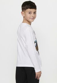 Wit t-shirt met lange mouwen voorzien van een kleurrijke grafische print op de voorkant. Zachte textuur en een relaxte pasvorm. Gecombineerd met zwarte broeken.