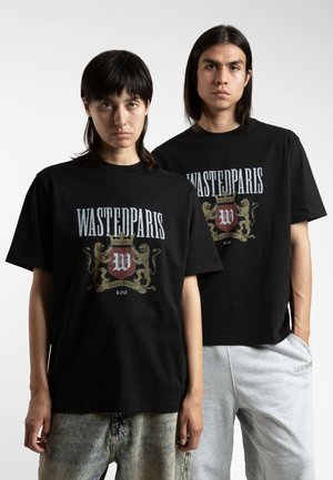 Black cotton t-shirts with front graphic featuring "WASTEDPARIS" and a coat of arms. Models wear relaxed-fit styles; one in grey pants.