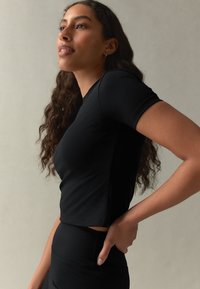 Svart figurnära kortärmad topp med rund halsringning, mjuk textur och något kortare modell, kombinerad med svarta leggings med hög midja.