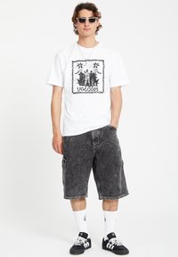 White graphic t-shirt with black print, paired with dark gray cargo shorts. Accessories include sunglasses and black sneakers with white accents.
