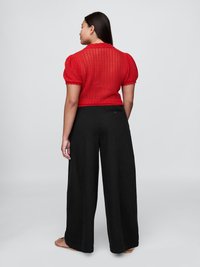 Top corto a maniche corte di colore rosso, realizzato in maglia, con un motivo testurizzato e un colletto rotondo, abbinato a pantaloni neri larghi. Il top presenta un design cropped.