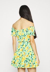 Abito floreale off-shoulder con una base verde e motivi di fiori gialli e arancioni. Maniche a ruota e gonna a strati.