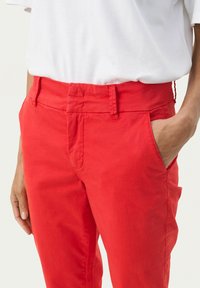 Rote Baumwollhosen zeichnen sich durch eine taillierte Taille, seitliche Taschen und eine glatte Textur aus. Das Design ist mit sauberer Nahtführung maßgeschneidert.