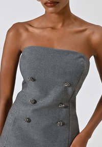 Abito grigio senza spalline con una texture a spina di pesce, caratterizzato da bottoni floreali argentati in un design doppiopetto. Silhouette liscia e aderente.