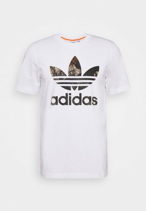 Camiseta blanca de algodón con un logo negro de Adidas que tiene un patrón de camuflaje en su interior. Mangas cortas y escote redondo.