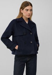 Marineblauer doppelt geknöpfter Peacoat aus Wolle, mit großen Knöpfen, einem Reverskragen und Seitentaschen, kombiniert mit dunklen Jeans.