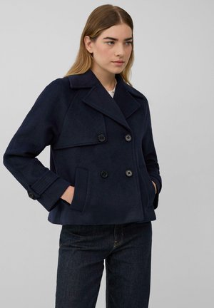 Marineblauwe double-breasted zeemanjas van wol, met grote knopen, een gelapte kraag en zijzakken, gecombineerd met donkere jeans.