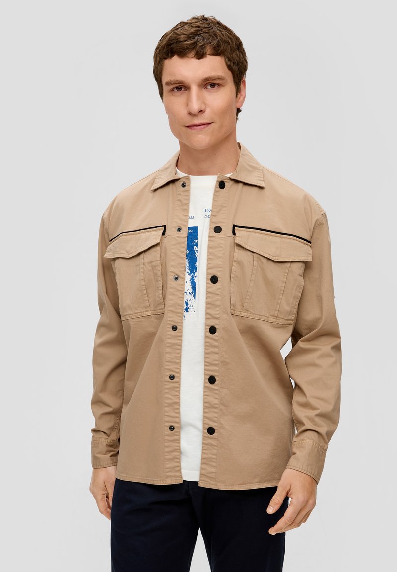 Giacca button-up color cammello con due tasche sul petto e dettagli neri. Realizzata in un tessuto morbido, presenta maniche lunghe e una vestibilità comoda.
