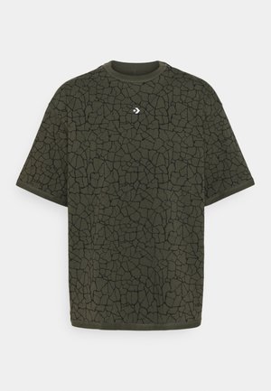 Oliwkowa koszulka z czarnym pękniętym wzorem, okrągłym dekoltem i krótkimi rękawami. Zawiera małe białe logo na klatce piersiowej.