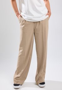 Beige wide-leg trousers with a smooth texture, front pleats, and side pockets, paired with black and white sneakers and a white t-shirt.