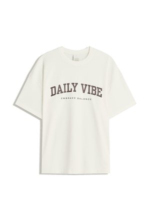 Witte katoenen t-shirt met gedurfde bruine tekst "DAILY VIBE" en kleinere tekst "EMBRACE BALANCE"; ontspannen, oversized pasvorm.