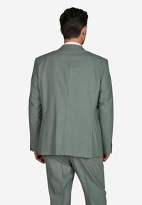 Lichtgroen pak met een gestructureerde stof, gekenmerkt door een enkele vent aan de achterkant en een getailleerde pasvorm. De broek komt overeen met het jack in kleur en stijl.