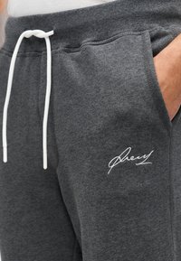 Γκρι βαμβακερές φόρμες με ελαστική μέση και κορδόνι, πλαϊνές τσέπες και λευκό κεντημένο λογότυπο στο αριστερό μπούτ ι. Μαλακή υφή.