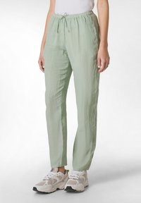Lichtgroene, lichte, gestructureerde broek met een elastische tailleband en verstelbare koord. Gedragen met chunky, beige mesh sneakers.