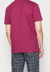 Kortærmet T-shirt i maroon bomuld, med en klassisk rund hals og en glat tekstur. Båret med mønstrede grå ternede bukser.