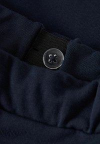 Granatowa tkanina o prążkowanej fakturze, z przezroczystym plastikowym guzikiem i elastyczną taśmą dla regulowanego dopasowania. Zbliżenie na detale paska.