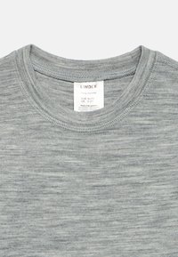 T-shirt in lana merino grigia con scollo rotondo, caratterizzata da una superficie morbida e strutturata. Include un'etichetta con informazioni sulle dimensioni e le modalità di cura.