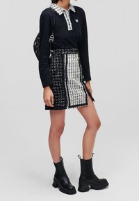 Polo nero a maniche lunghe con colletto testurizzato, abbinato a una mini gonna in tweed bianco e nero con uno spacco laterale e cuciture a contrasto. Stivali neri alla caviglia.