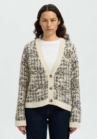Gestrickte Strickjacke in Creme und Braun mit V-Ausschnitt, gerippten Kanten und fünf großen braunen Knöpfen. Strukturmuster im gesamten Stoff.