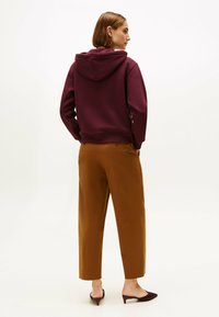 Bordeaux hætte sweatshirt parret med tan cropped bukser, der har lige snit og to baglommer. Fodtøj: bordeaux mule-sko.
