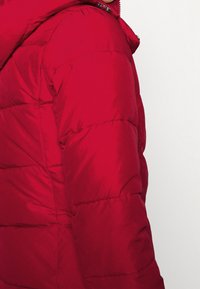 Roter gesteppter Mantel mit Kapuze, gesteppter Struktur, Reißverschluss und kleinen Metallakzenten am Reißverschluss.