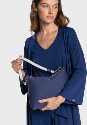 Bolso azul marino con acabado texturizado, asa de cuerda y detalles en dorado. El diseño es angular con cierre superior de cremallera.