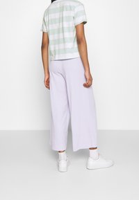 Pruhované pastelově zelené a bílé zkrácené tričko v kombinaci se širokými kalhotami světle levandulové barvy. Model nosí bílé tenisky a kotníkové ponožky.