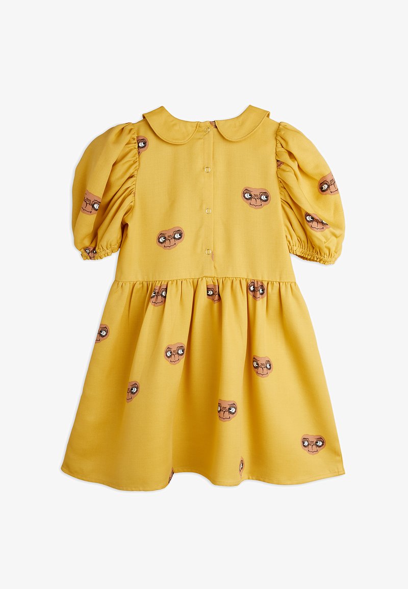 Kollane kleit puffvarrukatega, ümmarguse kaelusega ja nööbiga ees. Kangas on kaunistatud suurte silmadega trükitud nägude korduvate mustritega. Pehme tekstuur.