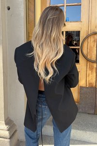 Schwarzer übergroßer Blazer mit offenem Rücken, strukturiertem Stoff und einem Bindegürtel in der Taille, kombiniert mit blauen Jeans.