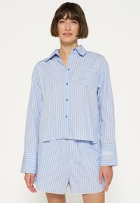 Conjunto de pijama a rayas azul claro hecho de tela suave, que incluye una camisa con botones y un bolsillo, y pantalones cortos a juego con mangas acanaladas.