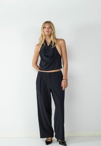 Black halter top with draped fabric, paired with wide-leg black trousers. Model wearing pointed-toe black shoes and a silver bracelet.