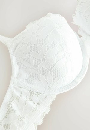 White lace bra with floral pattern, padded cups, and adjustable straps. Features intricate lace trim and textured mesh detailing.