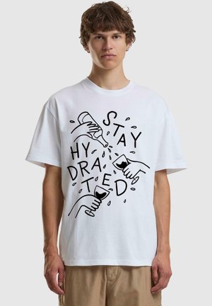 T-shirt en coton blanc avec un design graphique noir représentant des mains versant et tenant des boissons, accompagné du texte "RESTEZ HYDRATÉ."