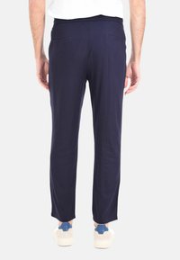 Pantaloni tapered blu navy con una texture liscia, dotati di tasche posteriori e una cintura comoda, abbinati a sneakers bianche e dettagli blu.