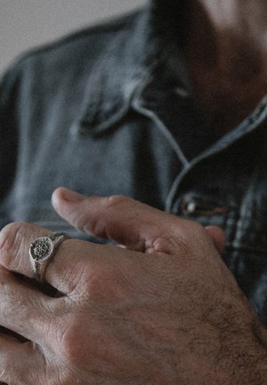 Bague en argent avec un design circulaire présentant un motif étoilé, sur un fond texturé d'une main, partiellement cachée par une veste en denim.