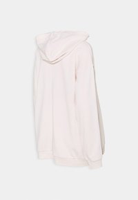 Hoodie overdimensionato di colore bianco sporco, visto da dietro, con un ampio cappuccio e maniche lunghe con polsini e orlo a coste.